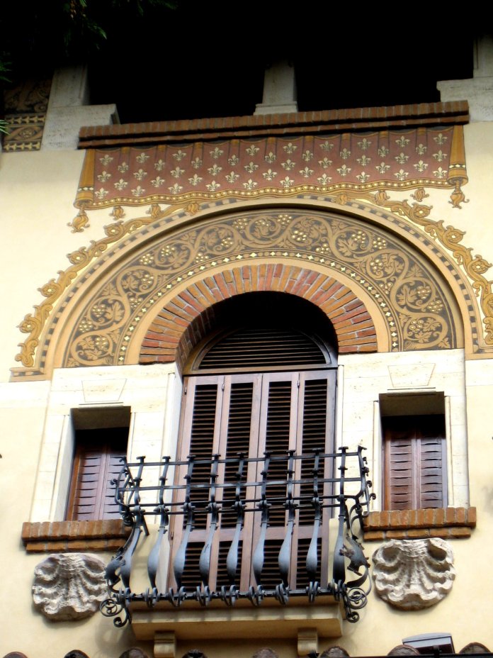 Juxtaposition de motifs décoratifs : peinture au-dessus de l'arc de la porte-fenêtre, ferronnerie de l'escalier, coquilles sous les fenêtres latérales.